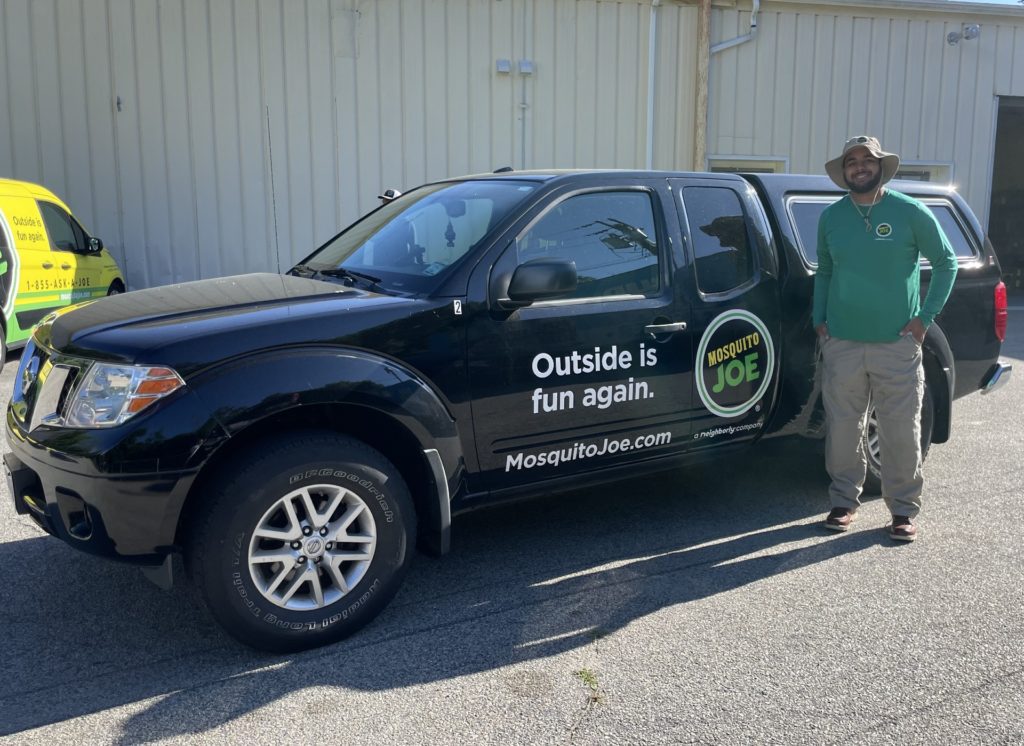 Cristian, Mosquito Joe of Northern Fairfield County field technician, standing in front of black Mosquito Joe truck ready to help our neighbors take back their yard from pesky outdoor pests in CT!
