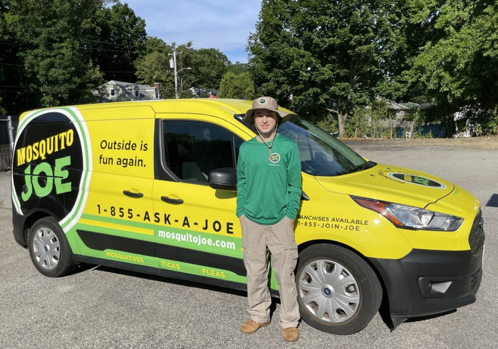 Jess, Field Technician that works at Mosquito Joe of Northern Fairfield County wearing uniform standing in front of yellow and green MoJo van.
