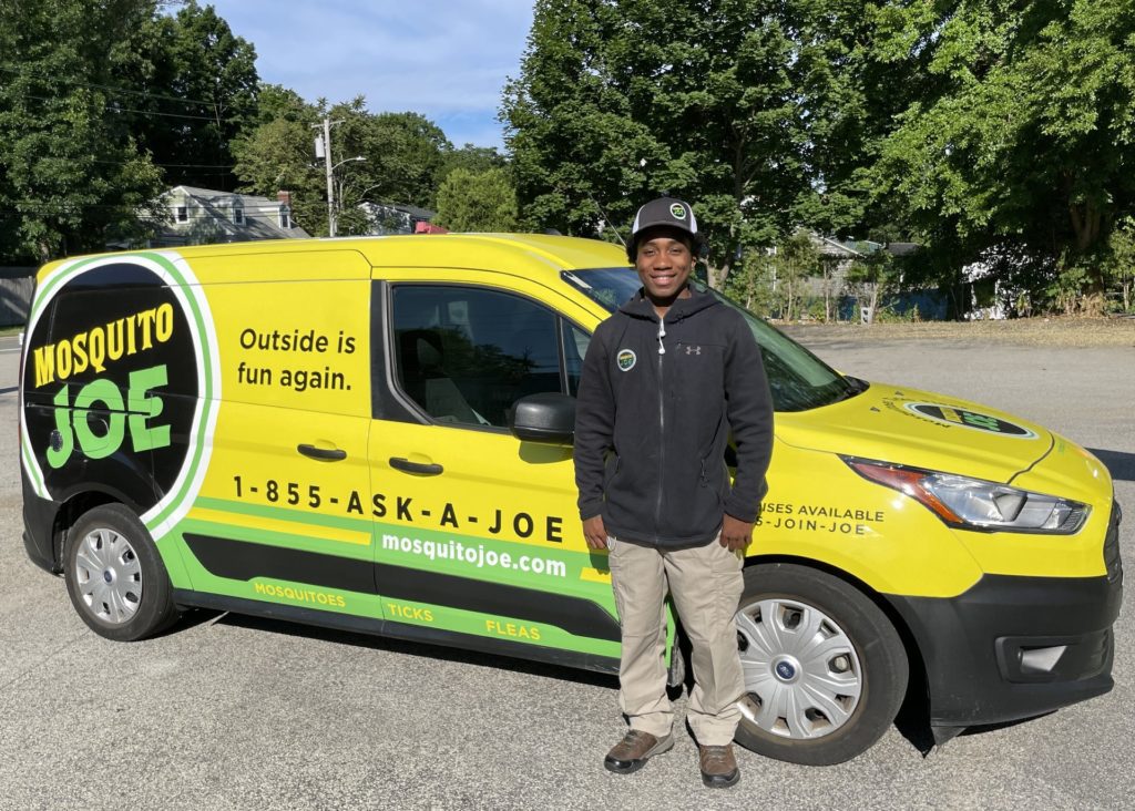  Nate, Field Technician, for Mosquito Joe of Northern Fairfield County wearing uniform standing in front of Mosquito Joe yellow and green van. 